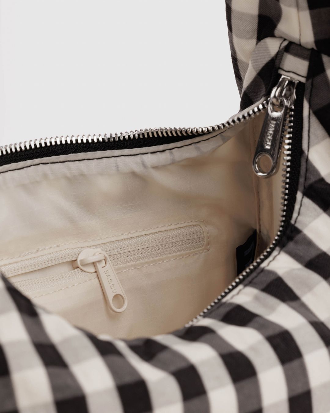 Baggu Meringue Bag Small - Black and Cream Gingham. Close-up of checkered nylon bag with silver metal zipper, and view of cream interior lining with pocket.