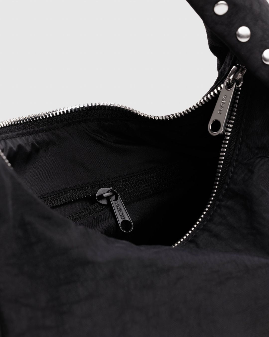 Baggu Meringue Bag Small - Studs. Close-up of black nylon bag with silver metal zipper, and view of black interior lining with pocket.