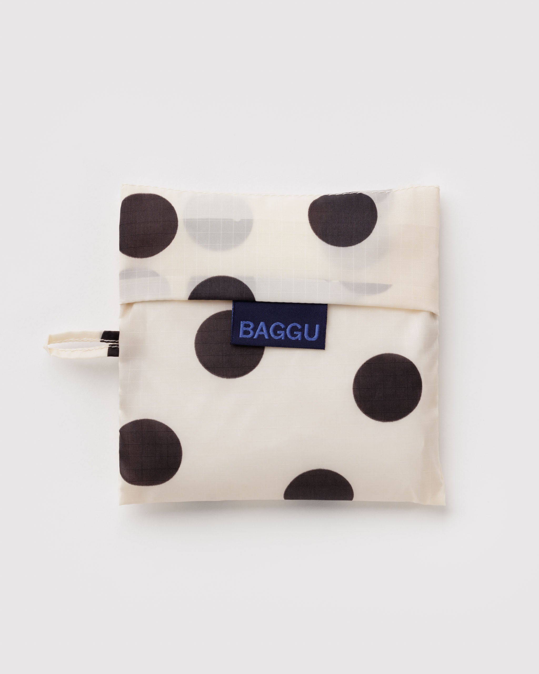 Standard Baggu Bag -  Black and Cream Polka Dot. Reusable shopping tote folded up in its compact square case with 'BAGGU" logo tag.