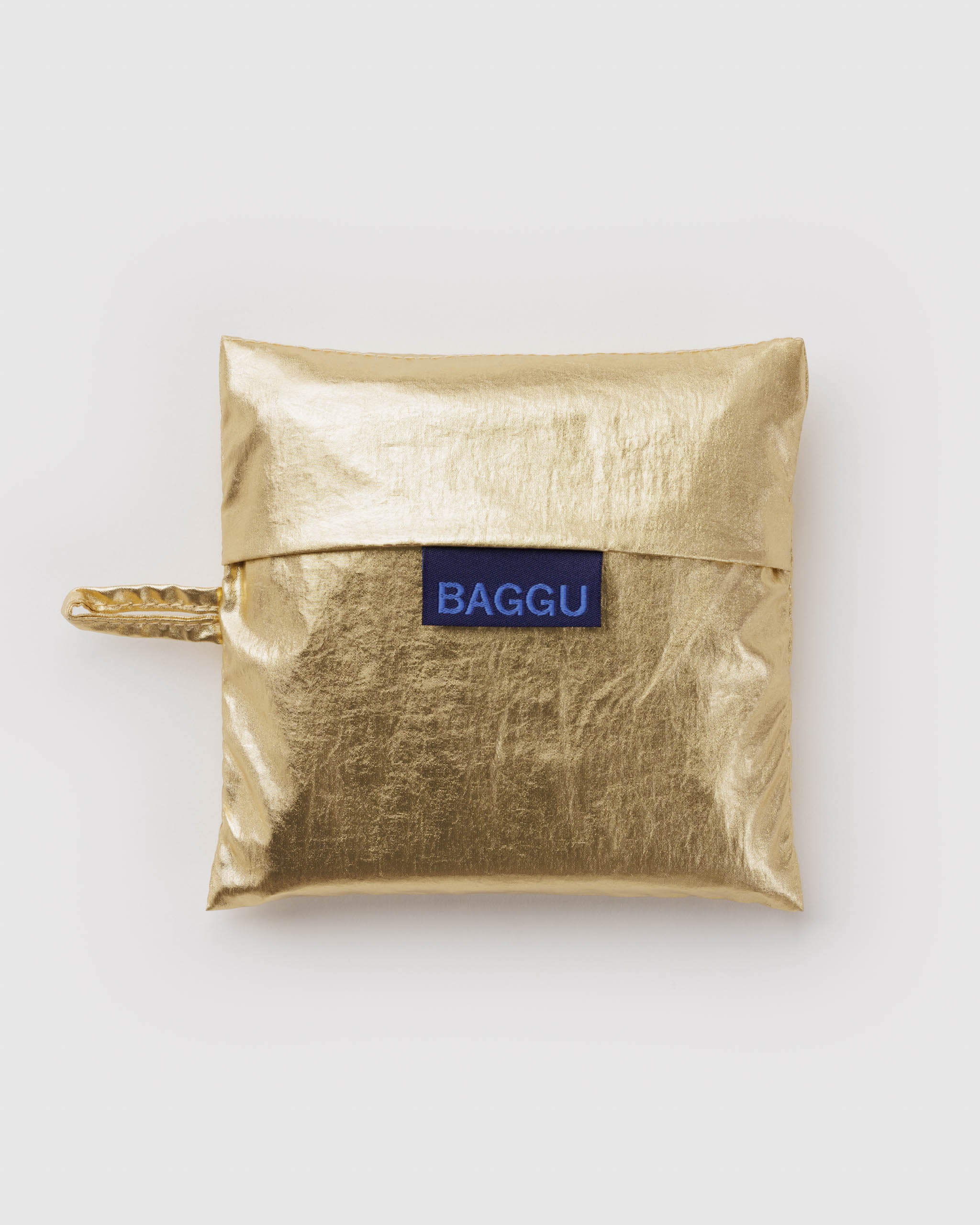 Standard Baggu Bag - Gold Metallic. Reusable shopping tote folded up in compact square case with 'BAGGU" logo tag.