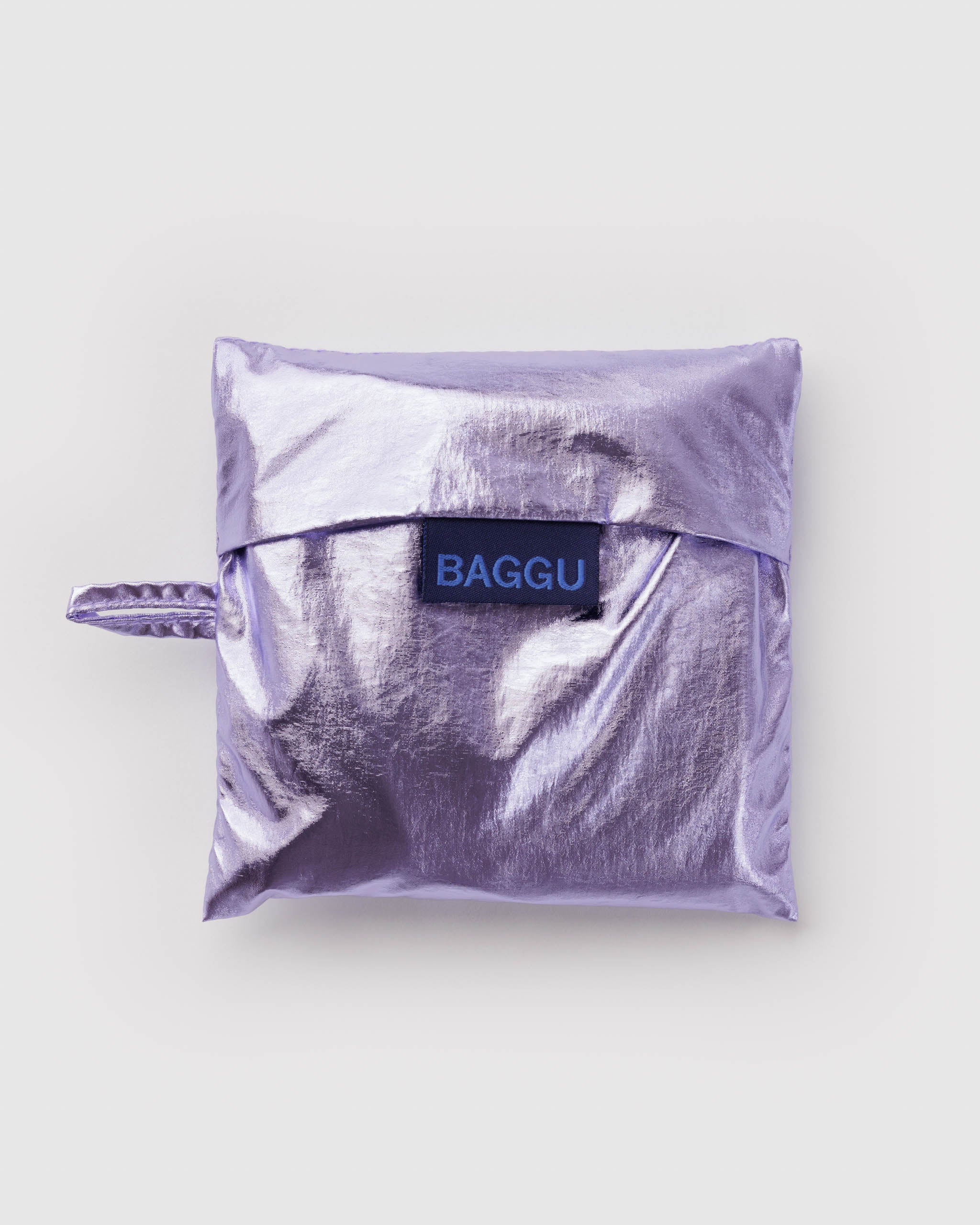 Standard Baggu Bag -  Lavender Metallic. Reusable shopping tote folded up in compact square case with 'BAGGU" logo tag.