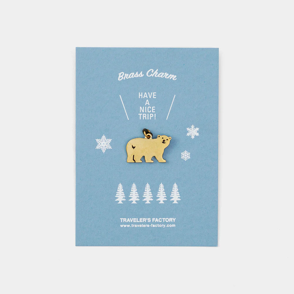 Bear-shaped brass charm on a blue card with snowflakes and trees, branded 'Traveler's Factory'.