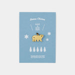 Bear-shaped brass charm on a blue card with snowflakes and trees, branded 'Traveler's Factory'.