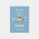 Bear-shaped brass charm on a blue card with snowflakes and trees, branded 'Traveler's Factory'.